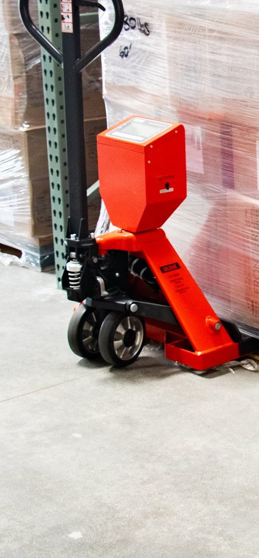 A pallet-scale jack in front of wrapped, weighed pallets ready for outbound freight to Amazon.
